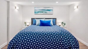 A bedroom with a large bed, a headboard, two bedside tables with lamps, a wall-mounted painting, and a white ceiling. - The Owlet Nwcalgary Queenbd Privatesuite (Calgary)