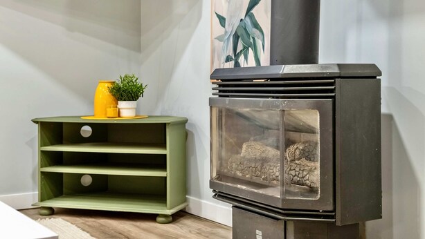 A room with a black wood-burning stove, a green shelving unit, and a yellow vase with a plant. - The Owlet Nwcalgary Queenbd Privatesuite (Calgary)