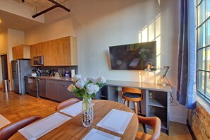A modern kitchen with wooden cabinets, a stainless steel refrigerator, and a flat-screen TV mounted on the wall. - Chic Ultramodern Studio Loft w/ Designer Features (Saint Louis)