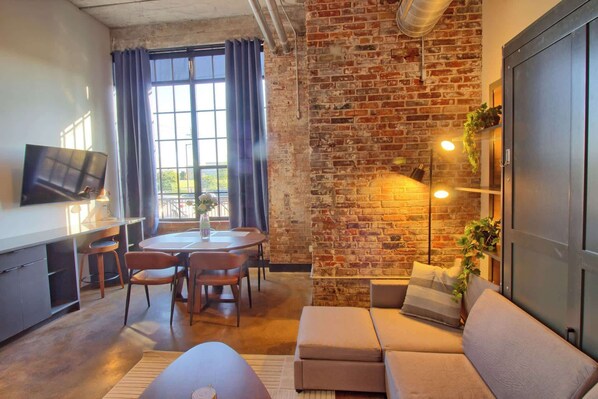 A modern living room with a brick wall, a sofa, a dining table with chairs, and a TV.