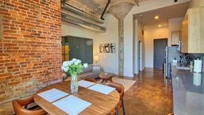 Una cocina moderna con electrodomésticos de acero inoxidable, una zona de comedor con una mesa de madera y sillas de cuero, y una pared de ladrillo.