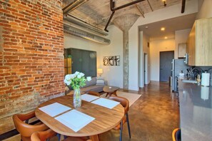 Une cuisine moderne dotée d’appareils électroménagers en acier inoxydable, un coin repas avec une table en bois et des chaises en cuir, et un mur en briques.