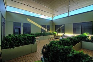 A covered outdoor area with seating, planters, and large windows.
