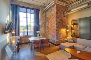 Un salon moderne avec un mur en briques, un coin repas comprenant une table et des chaises, un canapé et un téléviseur à écran plat fixé au mur.