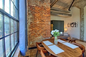 A modern meeting room with a brick wall, large windows, and a wooden table with chairs. - Chic Ultramodern Studio Loft w/ Designer Features (Saint Louis)