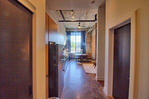 A hallway with a wooden floor, a dining area with a table and chairs, and a large window with curtains. - Chic Ultramodern Studio Loft w/ Designer Features (Saint Louis)
