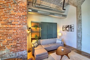 A modern living room with a brick wall, a grey sofa, a wooden coffee table, and abstract wall art. - Chic Ultramodern Studio Loft w/ Designer Features (Saint Louis)