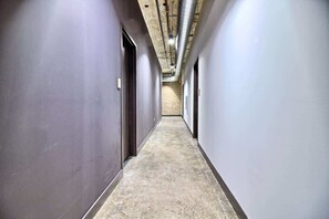 A long, narrow hallway with grey walls and a concrete floor, leading to a door at the end.