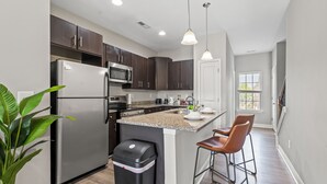 A modern kitchen with dark cabinets, stainless steel appliances, a granite countertop, and pendant lighting. - Upscale King 3BR Townhouse in Pineville (Pineville)