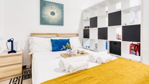 Una habitación de hotel moderna con una cama, una mesita de noche con lámpara, una obra de arte grande en la pared y un armario empotrado con estantes.