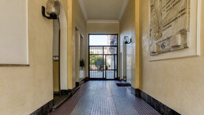 Un pasillo con suelo de baldosas, un portón negro al final y una placa en la pared.