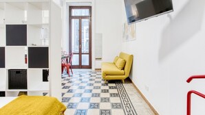 Una habitación con un sofá, un televisor en la pared y un suelo estampado.
