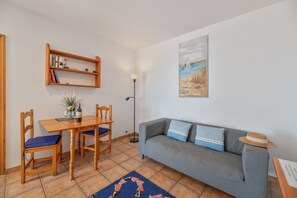 Una sala de estar con una mesa de comedor, sillas, un sofá, una estantería y un cuadro en la pared.
