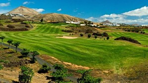 A golf course with well-maintained fairways, bunkers, and a clear sky.