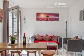 A living room with a red sofa, a wooden dining table, and a painting of a field with a tree.