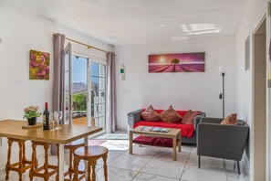 A living room with a sofa, a table with a bottle and glasses, a chair, and a painting on the wall.