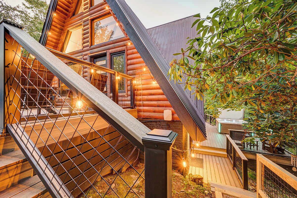 A log cabin with a wooden staircase leading to a deck, surrounded by trees.