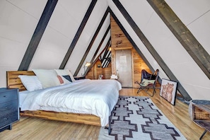 A bedroom with a sloped ceiling, wooden beams, a bed with white bedding, a chair, and a rug. - A-Frame Ski-In/Out Hot Tub Game Room, Walk to Town (Beech Mountain)