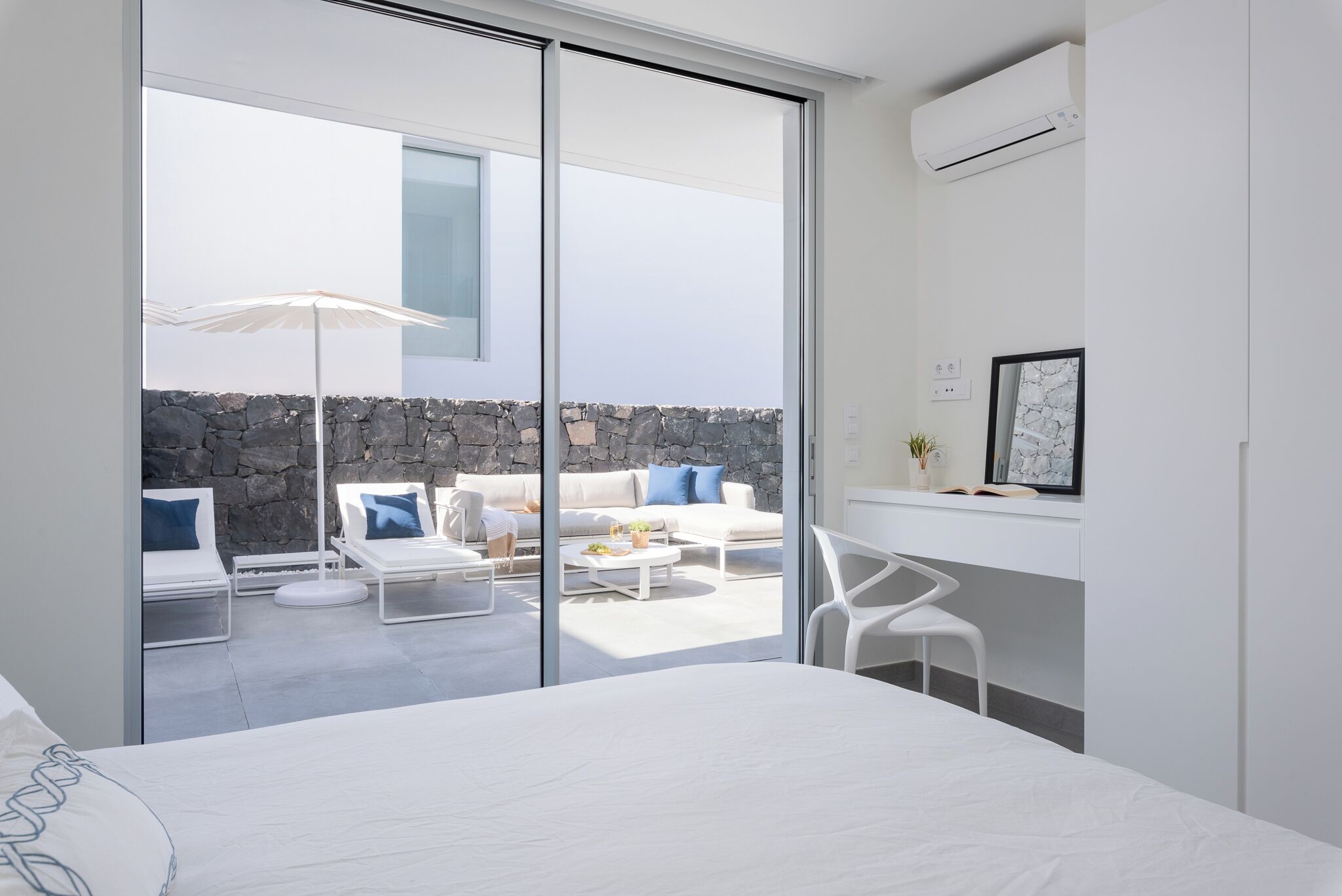 Une chambre d’hôtel moderne avec un grand lit, un balcon doté de meubles blancs et un mur en pierre.