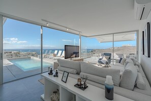 Een moderne woonkamer met een groot raam, uitzicht op een zwembad en een comfortabele zithoek.