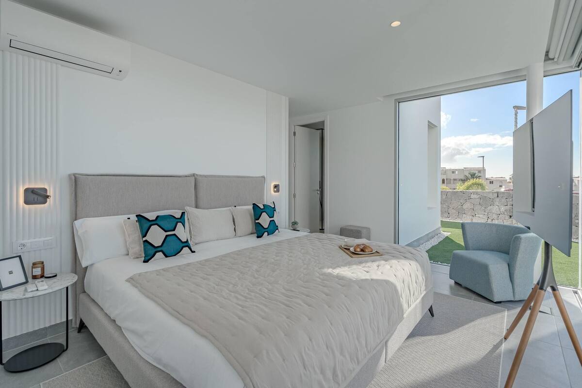 A modern hotel room with a large bed, a view of the city, and a balcony with a chair.