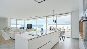 A modern kitchen with a large island, white cabinetry, and a view of the sea. - Casangular by Upper (Adeje)