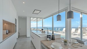 A modern kitchen with a large island, a dining area with a view of the ocean, and a minimalist design. - Casangular by Upper (Adeje)