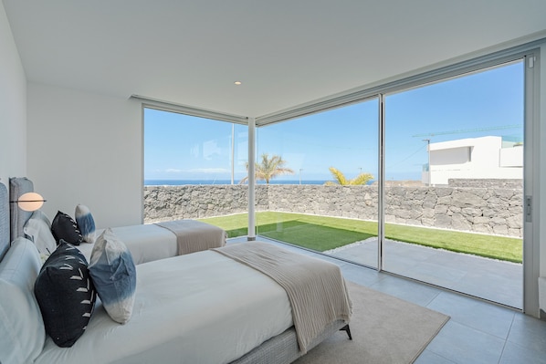 Een moderne slaapkamer met een grote glazen deur die leidt naar een balkon met een stenen muur en uitzicht op de oceaan.