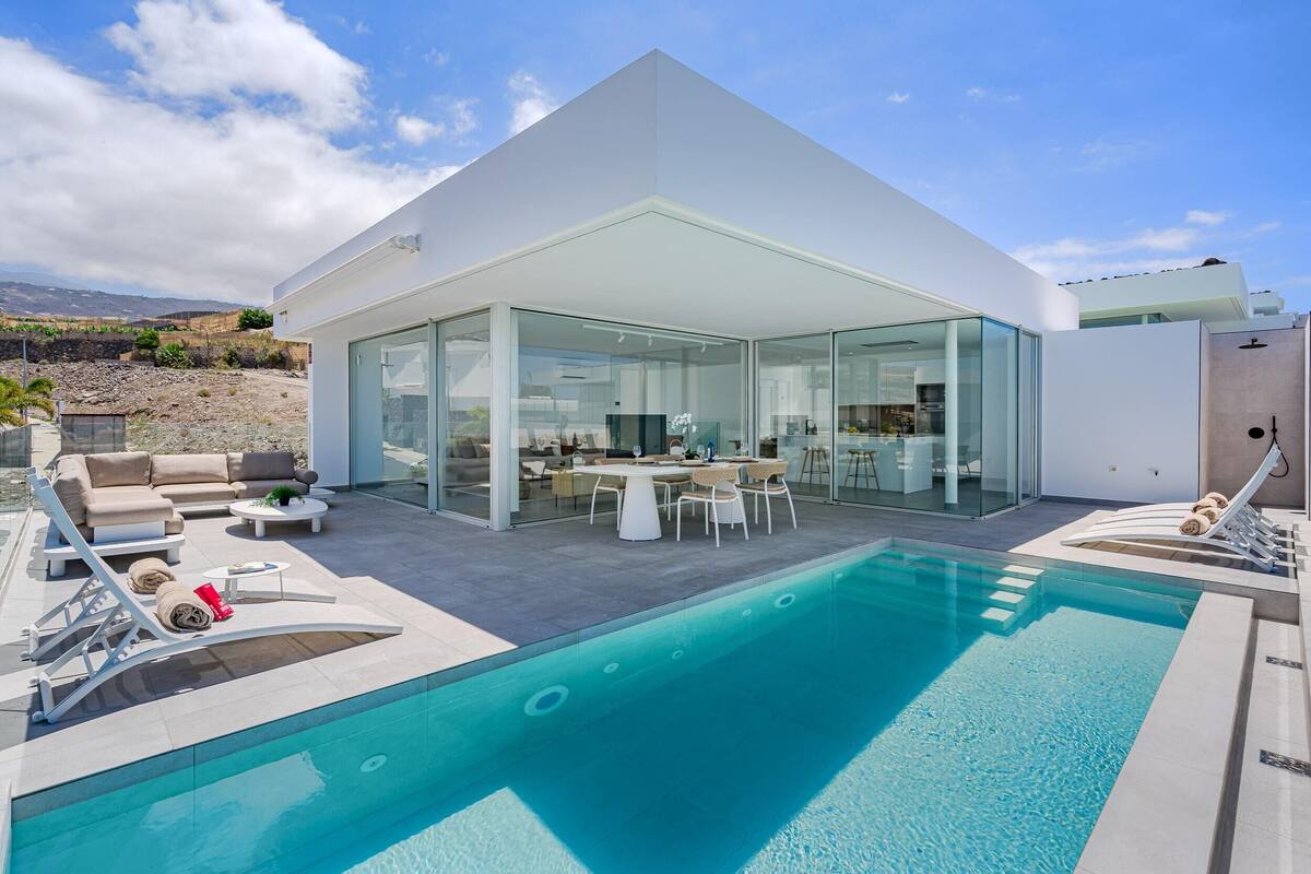 A modern house with a swimming pool, outdoor seating, and a glass-enclosed dining area.