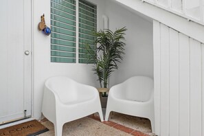 A white door with a 'WELCOME' mat, a potted plant, and two white plastic chairs.