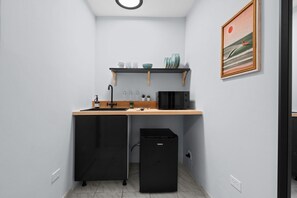 A compact kitchen with a sink, a microwave, a small refrigerator, and a shelf with dishes and cups. - Ocean Park Studio | Near Beach | Smart TV + Wi-Fi (San Juan)