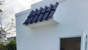 A white building with a tiled roof, a white door with a 'WELCOME' mat, a small white chair, a potted plant, and a white railing. - Ocean Park Studio | Near Beach | Smart TV + Wi-Fi (San Juan)