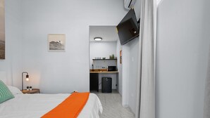A hotel room with a bed, an orange throw, a desk, and a kitchenette. - Ocean Park Studio | Near Beach | Smart TV + Wi-Fi (San Juan)