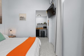 A hotel room with a bed, an orange throw, a desk, and a kitchenette.