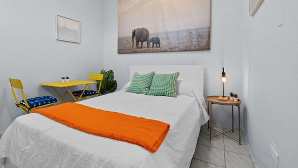 A bedroom with a bed, a desk, a chair, a nightstand, and a painting on the wall. - Ocean Park Studio | Near Beach | Smart TV + Wi-Fi (San Juan)