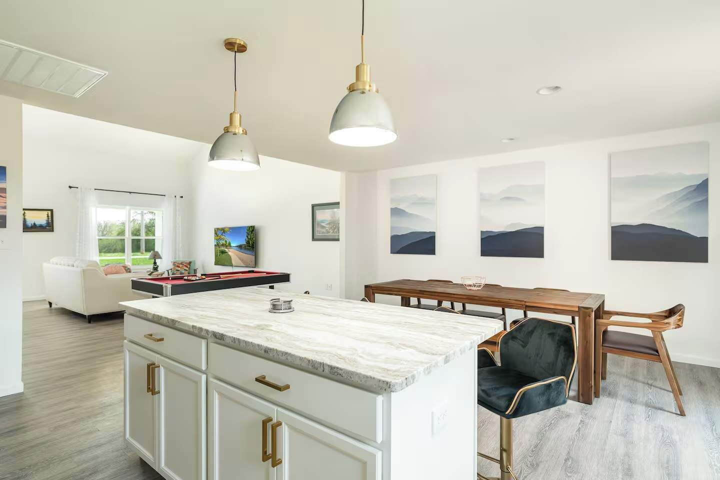 Cocina moderna con una isla de mármol, luces colgantes y un comedor con mesa y sillas de madera.