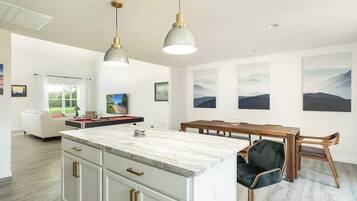 Cocina moderna con una isla de mármol, luces colgantes y un comedor con mesa y sillas de madera.