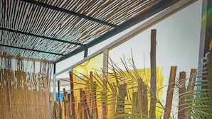 A covered outdoor seating area with bamboo walls, potted plants, and a clear view of the sky. - Eco Bay Surf Camp (Aourir)