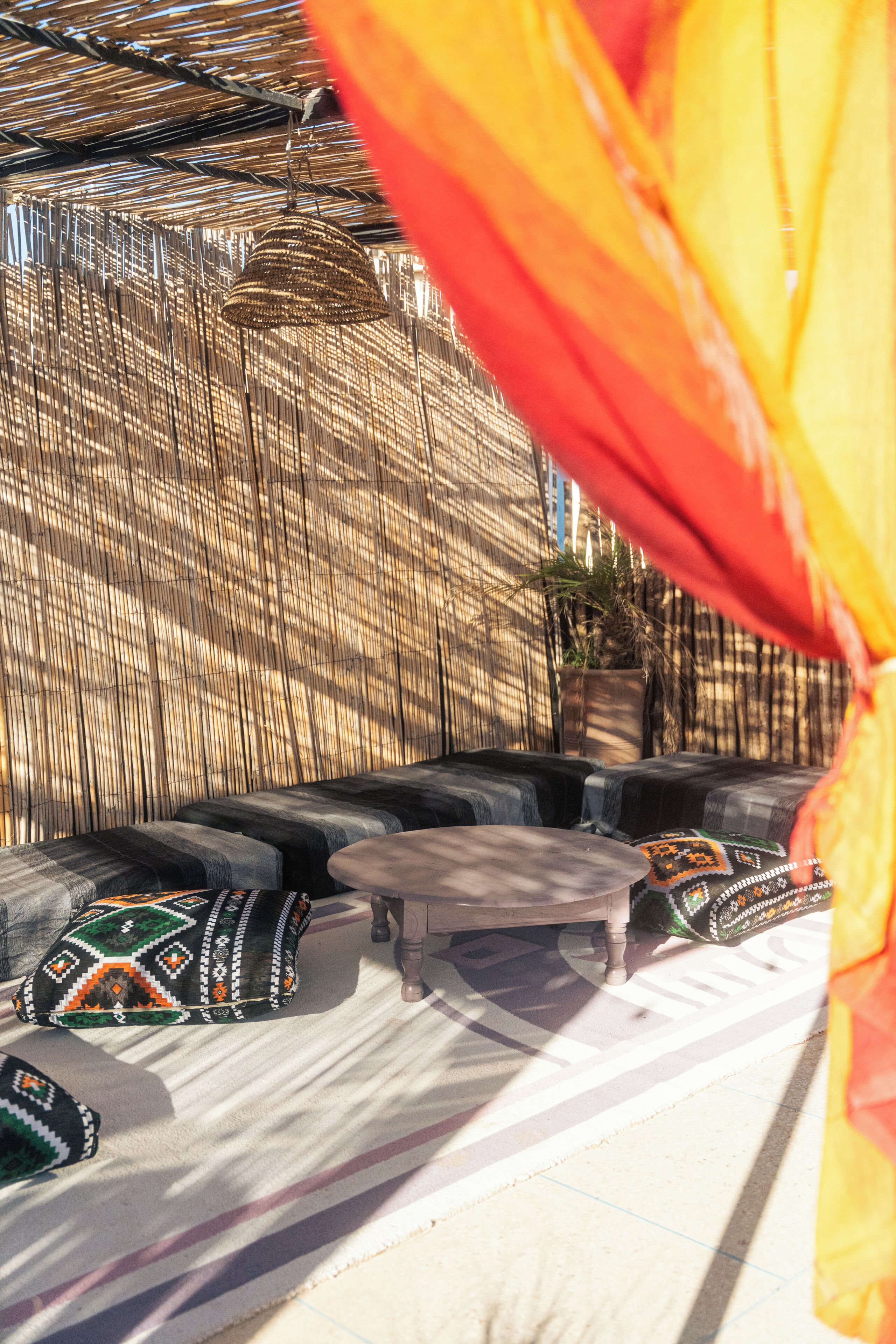 A seating area with a woven backdrop, a hanging light fixture, and a potted plant.