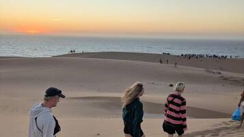 Cena de praia com pessoas caminhando na areia ao pôr do sol.
