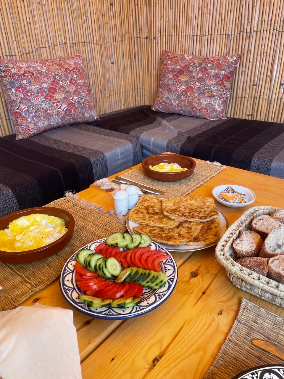 Una mesa de comedor con diversos alimentos, incluyendo un plato de vegetales cortados, un bol de huevos y varias piezas de pan plano.