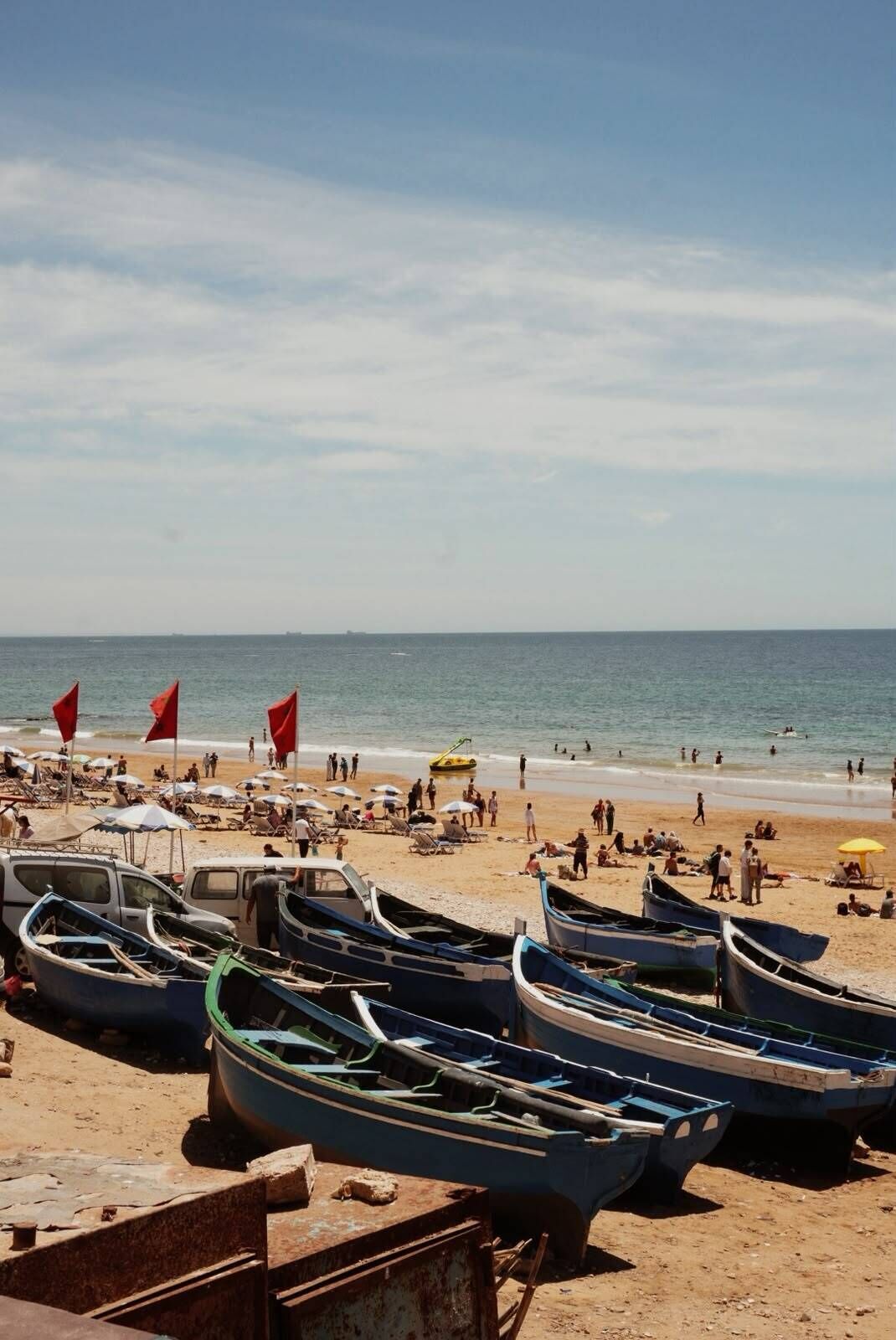 A beach with several boats parked on the sand, a clear sky, and people enjoying the beach.