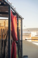 Un paño rojo colgado de una estructura metálica, posiblemente una barandilla de balcón, con un cielo despejado y edificios lejanos al fondo.