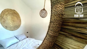 A room with a woven hanging chair, a woven wall hanging, and a bed with white bedding. - Eco Bay Surf Camp (Aourir)