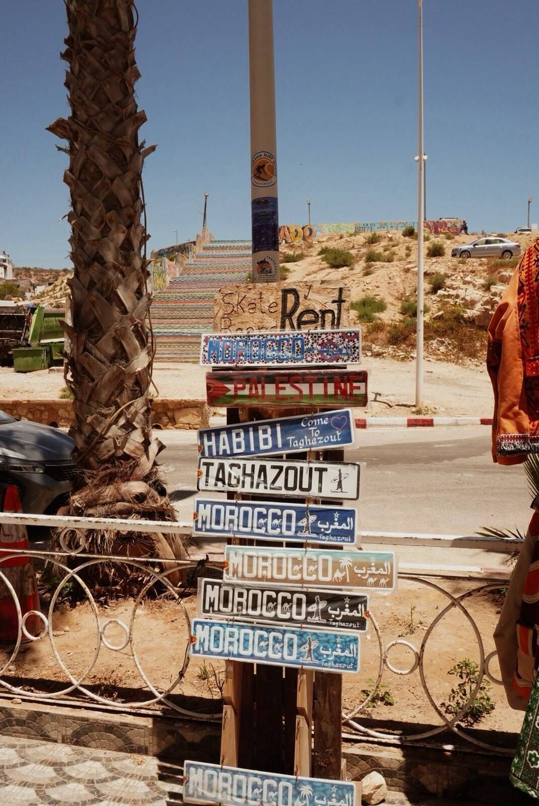 Eine Auswahl von Schildern mit Destinationen wie 'Palestine', 'Habibi', 'Taghazout' und 'Marokko' in verschiedenen Sprachen.
