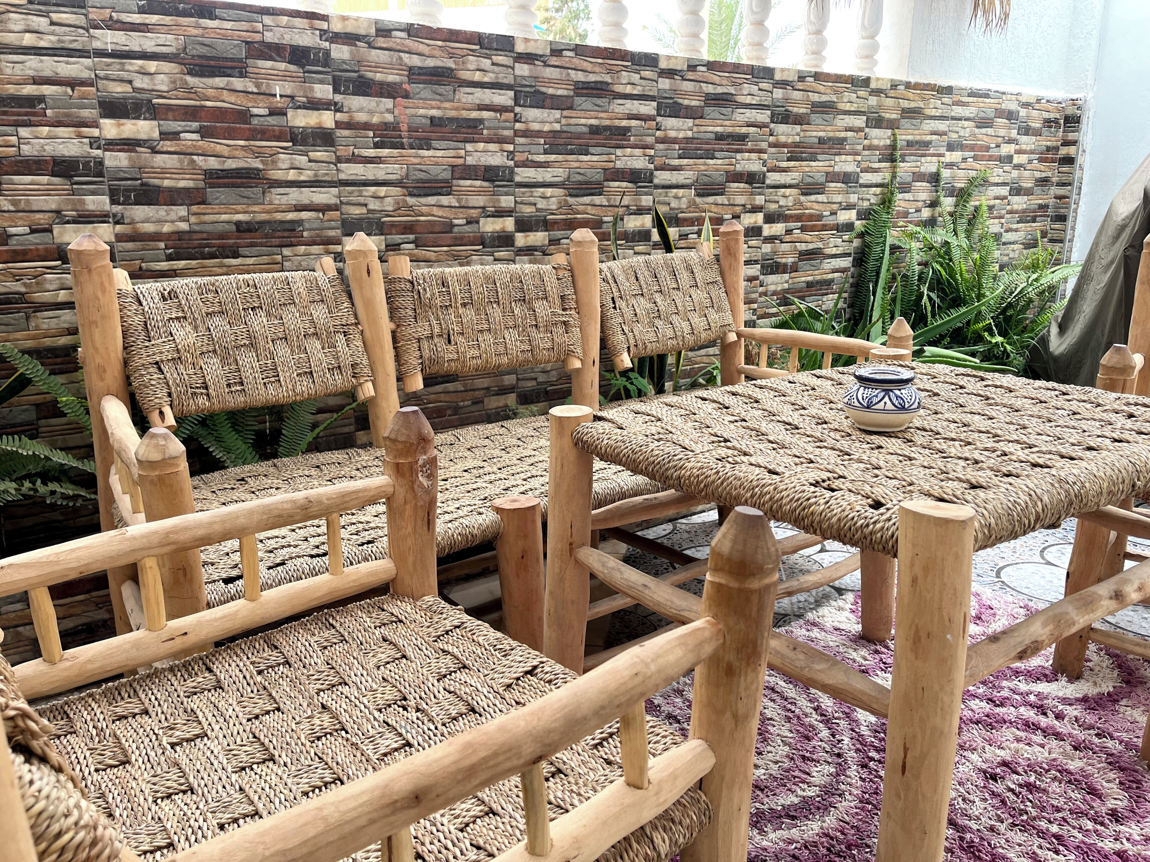 Wicker furniture with a woven seat and backrest, a woven table, and a stone-patterned wall.