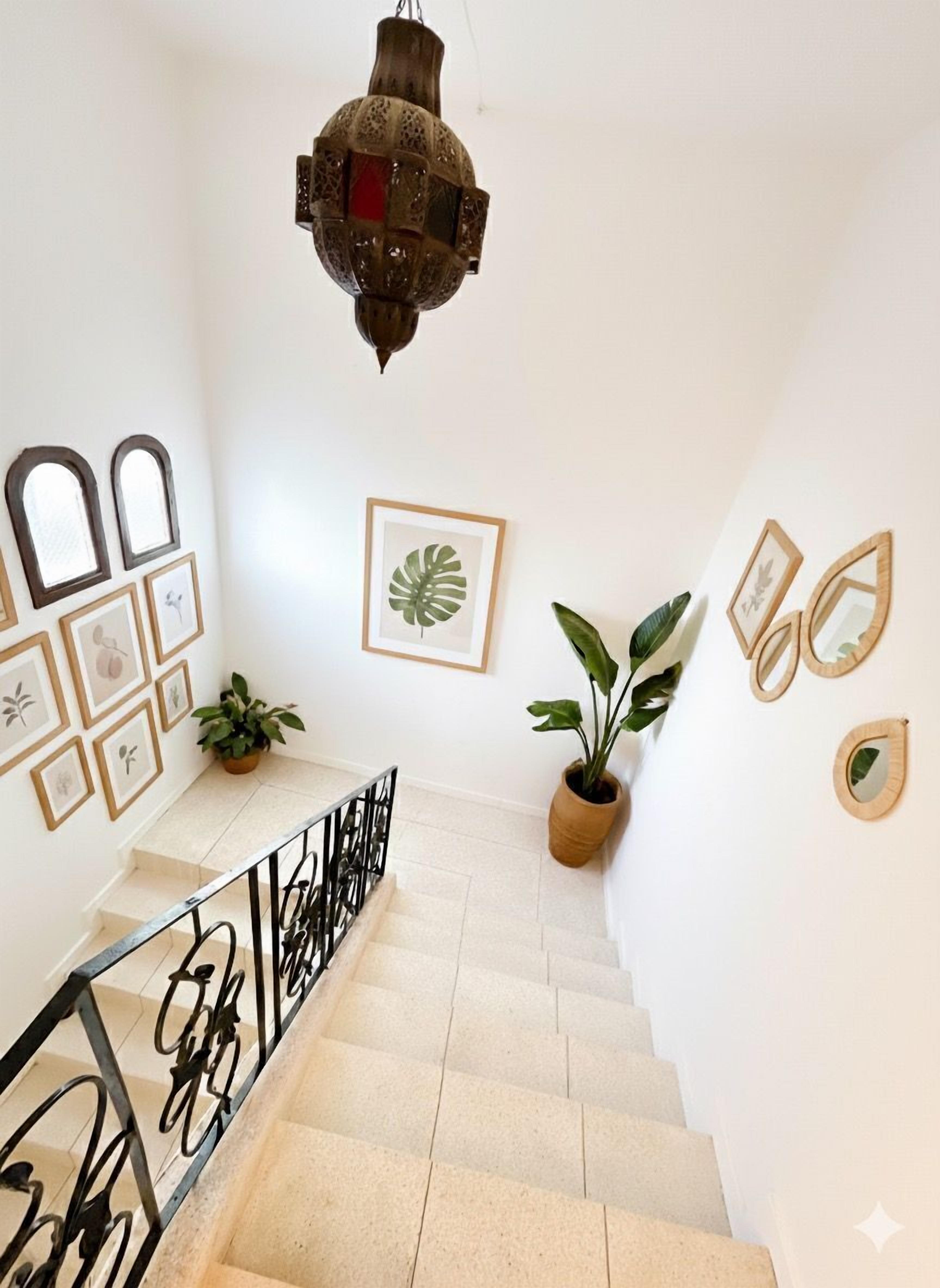 A staircase with a metal railing, surrounded by framed artwork and potted plants.