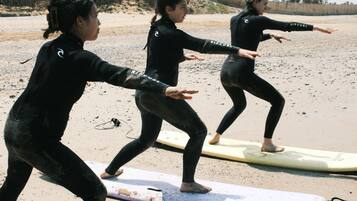 Drie mensen oefenen op surfplanken aan een zandstrand.
