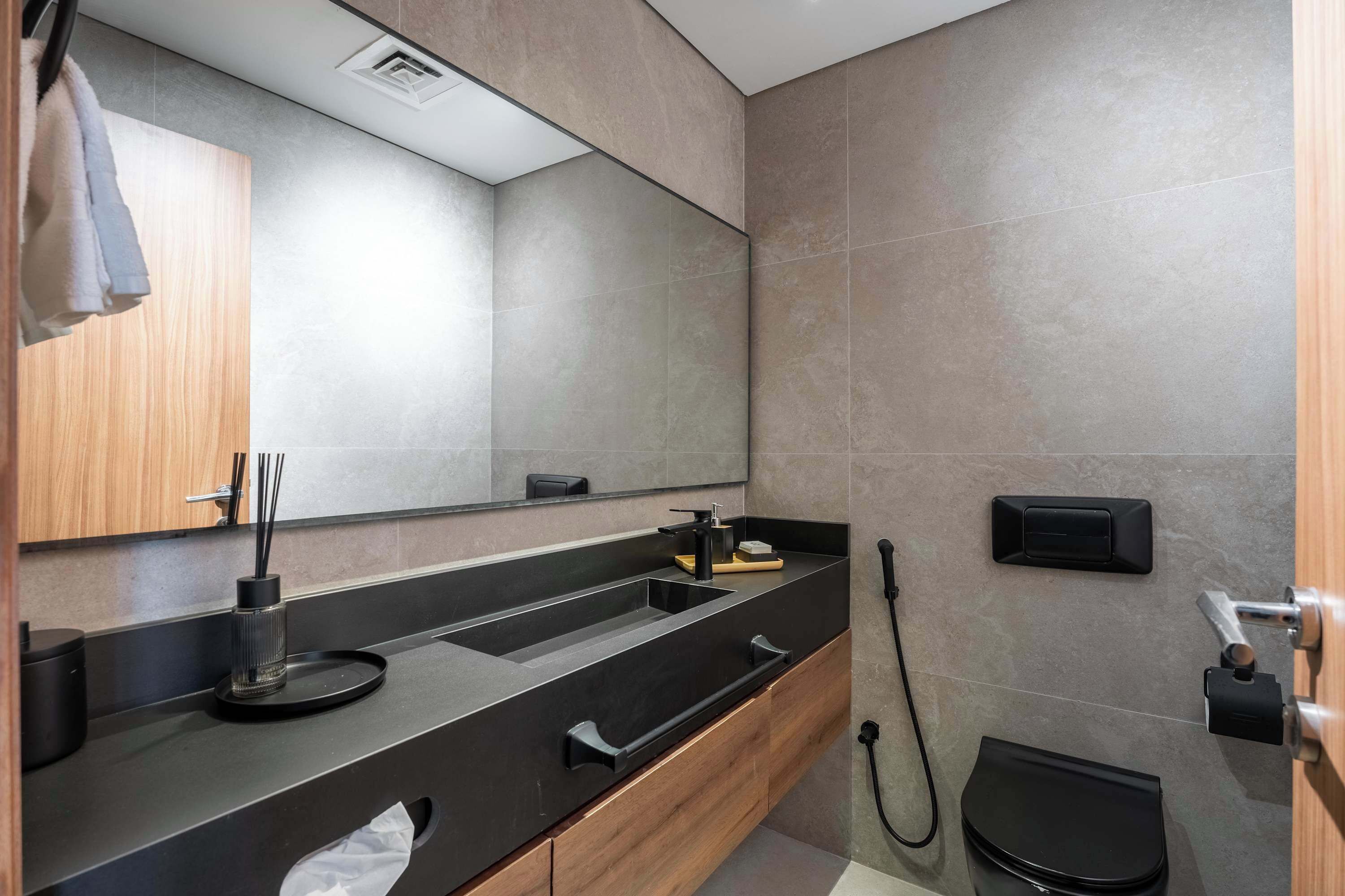 Een moderne badkamer met een grote spiegel, een zwarte wastafel, houten kastjes en een toilet.
