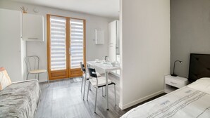 A bedroom with a bed, a desk with a chair, a nightstand, and a window with blinds. - Studio Apartment 'Le Laurier' with Private Terrace, Shared Garden and Wi-Fi (Lherm)